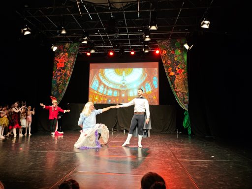 Tanzaufführung auf einer Bühne mit buntem Hintergrund und Tänzern in Kostümen.