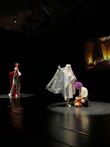 Drei Schauspieler auf der Bühne in historischer Kostümierung mit dramatischer Beleuchtung.