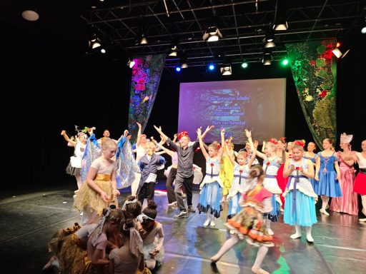 Bunt gekleidete Tänzer auf der Bühne feiern mit erhobenen Händen.