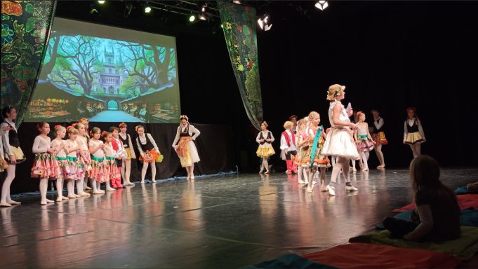 Bühne mit tanzenden Kindern in bunten Kostümen und einer kreativen Hintergrundprojektion.