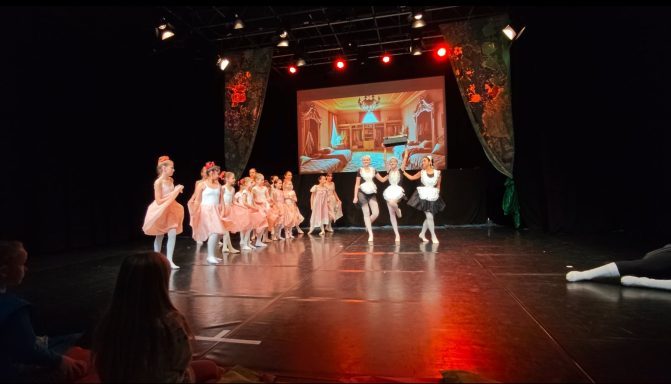 Tanzaufführung mit Mädchen in rosa Kostümen auf der Bühne. Im Hintergrund Projektion.