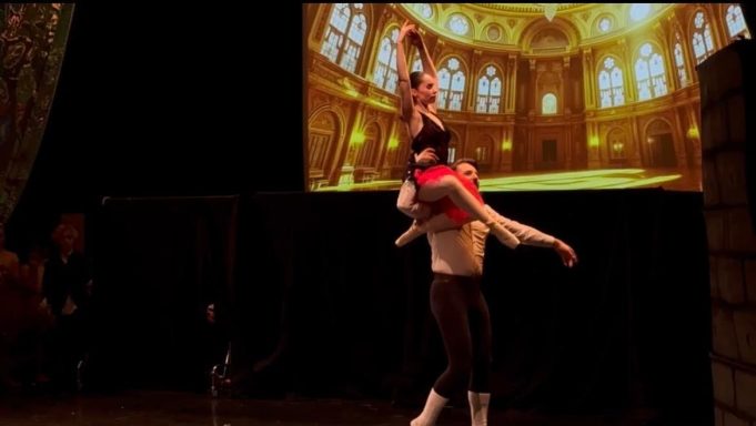 Tanzpaar hebt eine Balletttänzerin in einer eleganten Pose vor einer großen Fensterkulisse.