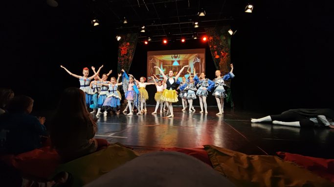 Tanzgruppe in bunten Kostümen auf einer Bühne mit bunten Lichtern.