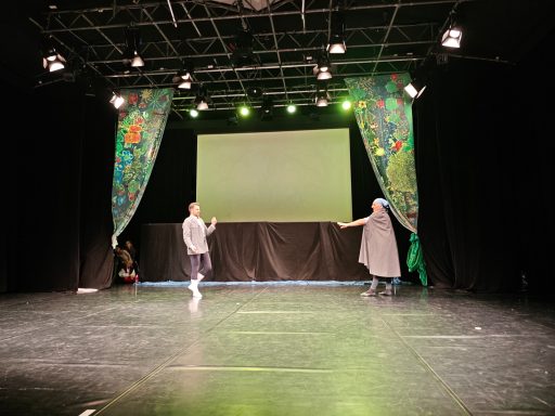 Zwei Tänzer auf einer Bühne mit bunten Vorhängen und einem grünen Lichtschein.