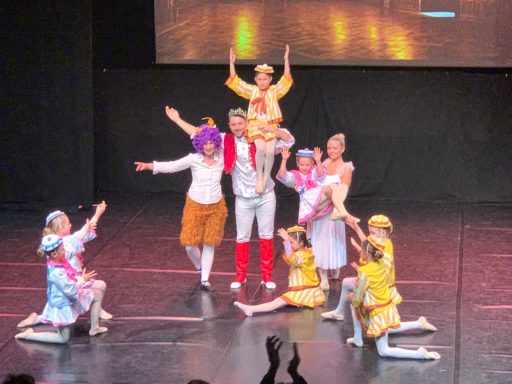 Bunt kostümierte Tänzer in einer fröhlichen Gruppenchoreographie auf der Bühne.