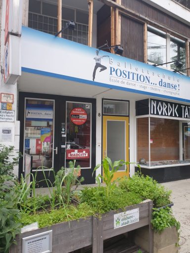 Geschäftsgebäude mit Werbung für "Position" und angrenzenden, leerstehenden Laden.