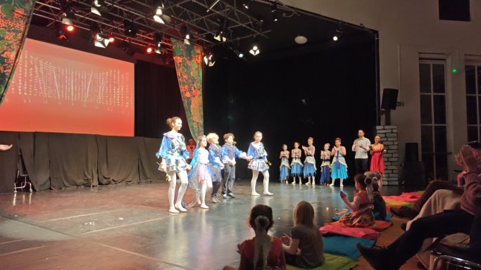 Tanzaufführung mit Tänzern in blauen Kostümen auf der Bühne vor einem Publikum.