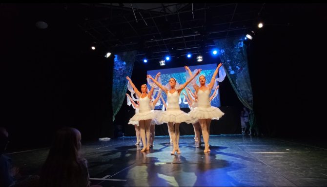 Vier Balletttänzerinnen in weißen Tutus stehen auf der Bühne und tanzen synchron.