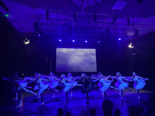Tänzerinnen in weißen Kleidern führen eine Choreografie vor blauer Lichtkulisse auf.