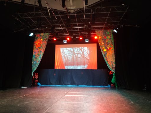 Bühne mit rotem Hintergrund, grüner Kulisse und farbigen Vorhängen. Beleuchtung in Rot.