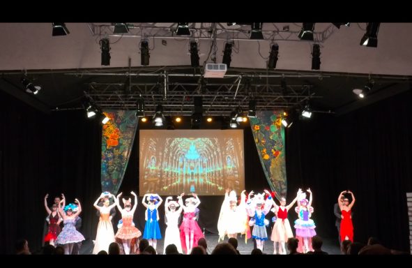 Eine Gruppe von Tänzern in Kostümen auf einer Bühne mit buntem Hintergrund.