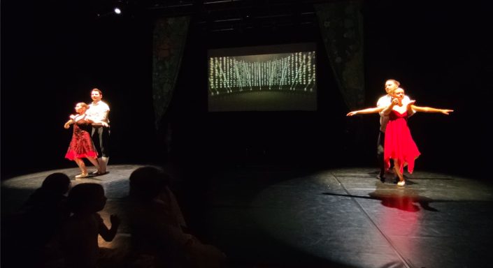 Tanzaufführung mit zwei Tänzern in roten Kostümen auf einer Bühne.