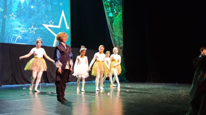 Tanzende Kinder in bunten Kostümen auf einer Bühnenaufführung.